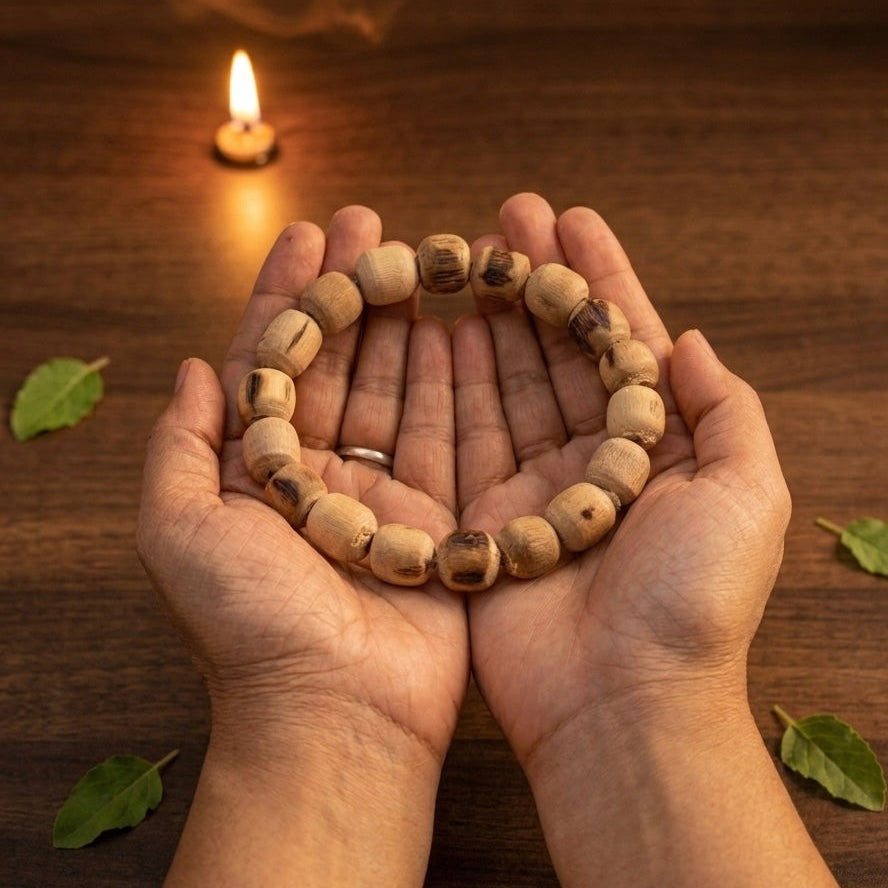 Hands holding a Tulsi beaded bracelet on a wooden surface with a candle in the background